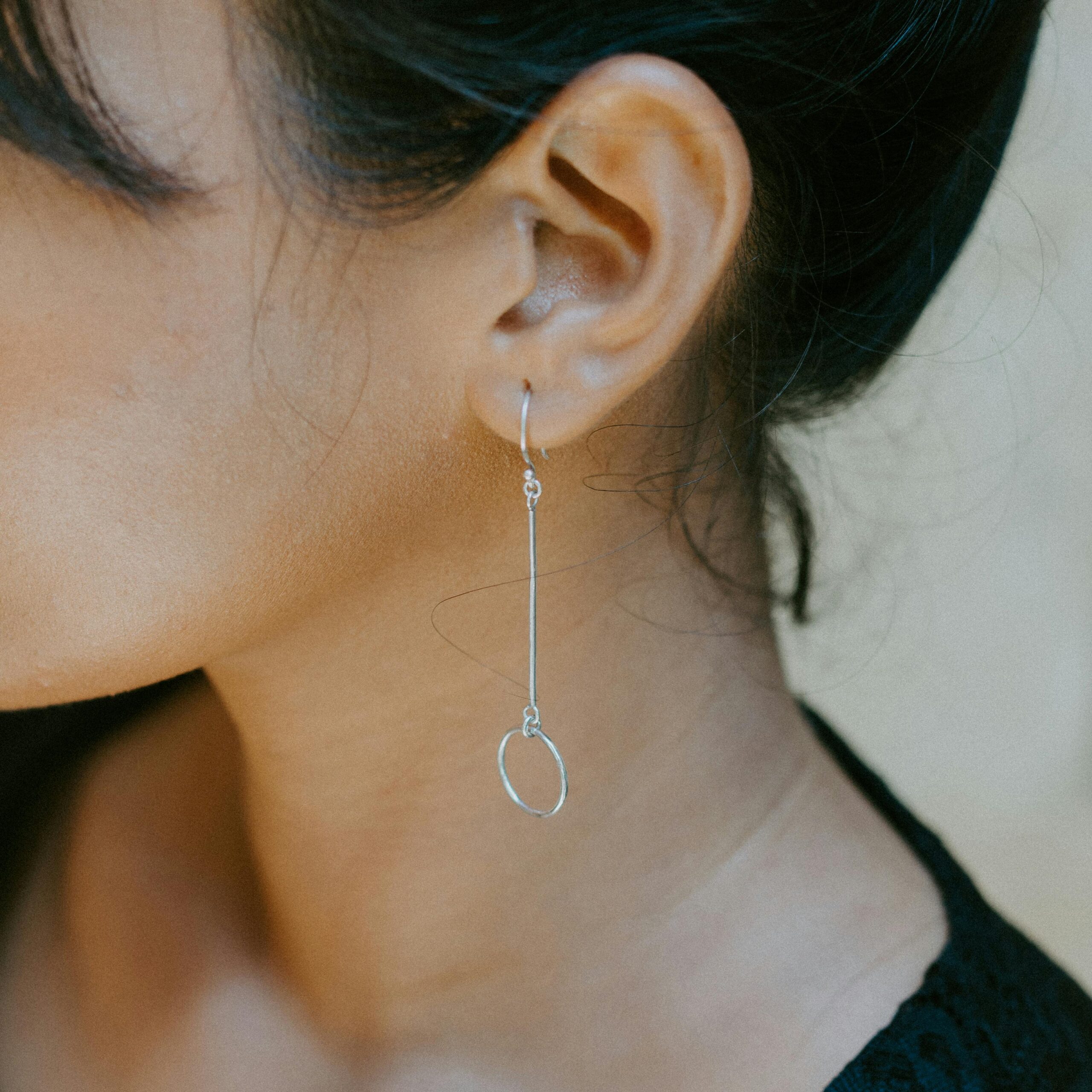 Close-up of a woman's ear showcasing a minimalist silver earring, highlighting modern jewelry design.